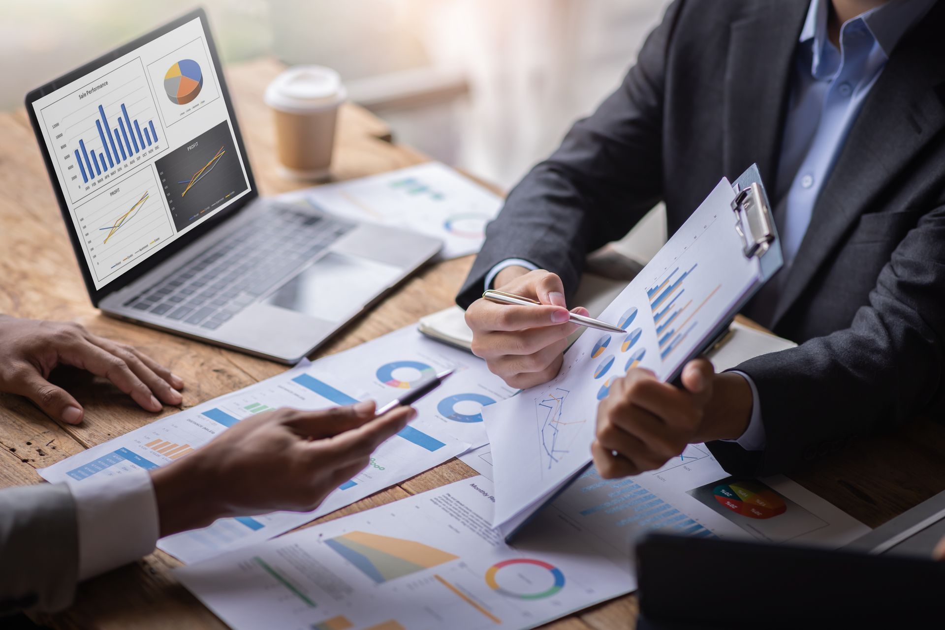 People reviewing charts and graphs in a business meeting at a desk with laptop and documents