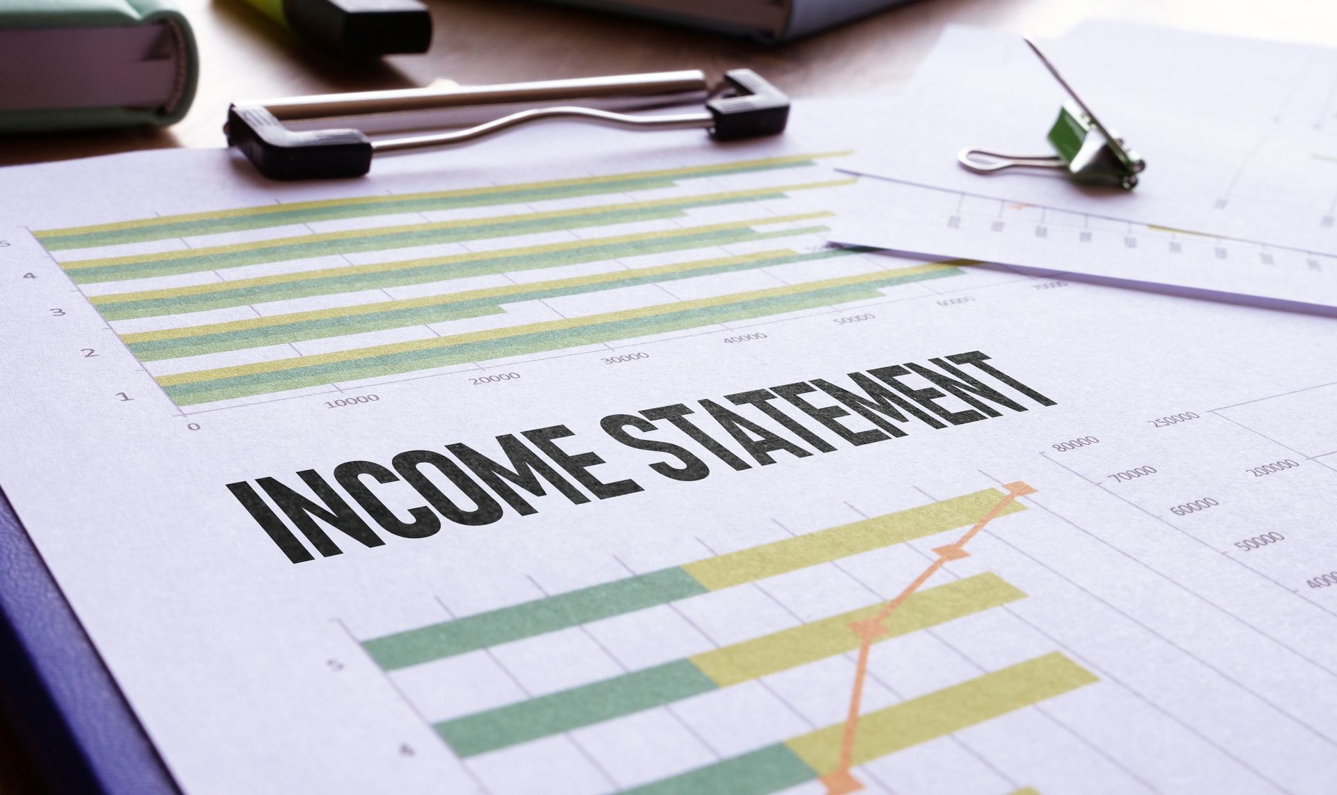 Income statement on a desk with charts, graphs, and a pen in the foreground
