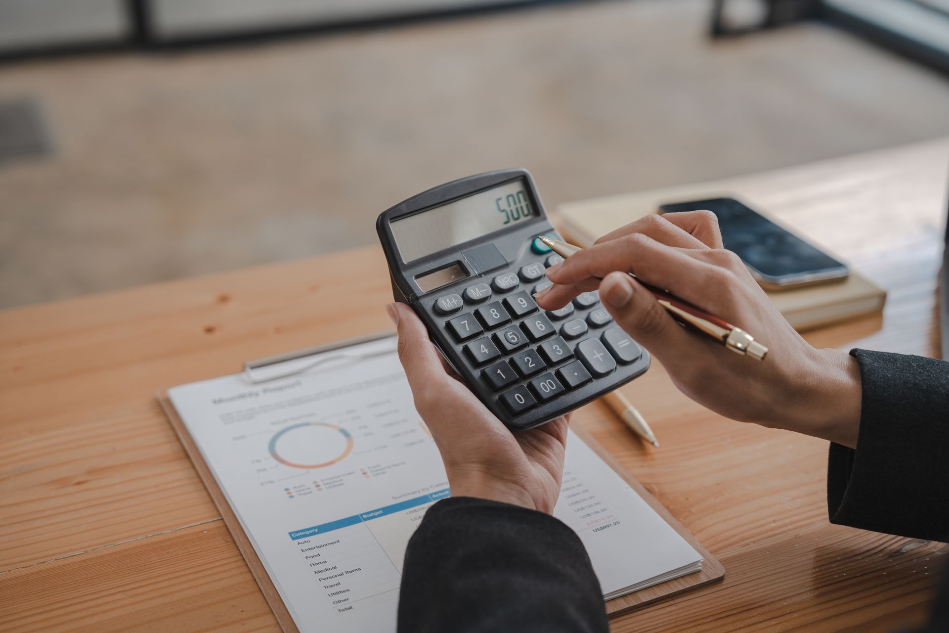 Person using a calculator beside printed charts on a wooden desk