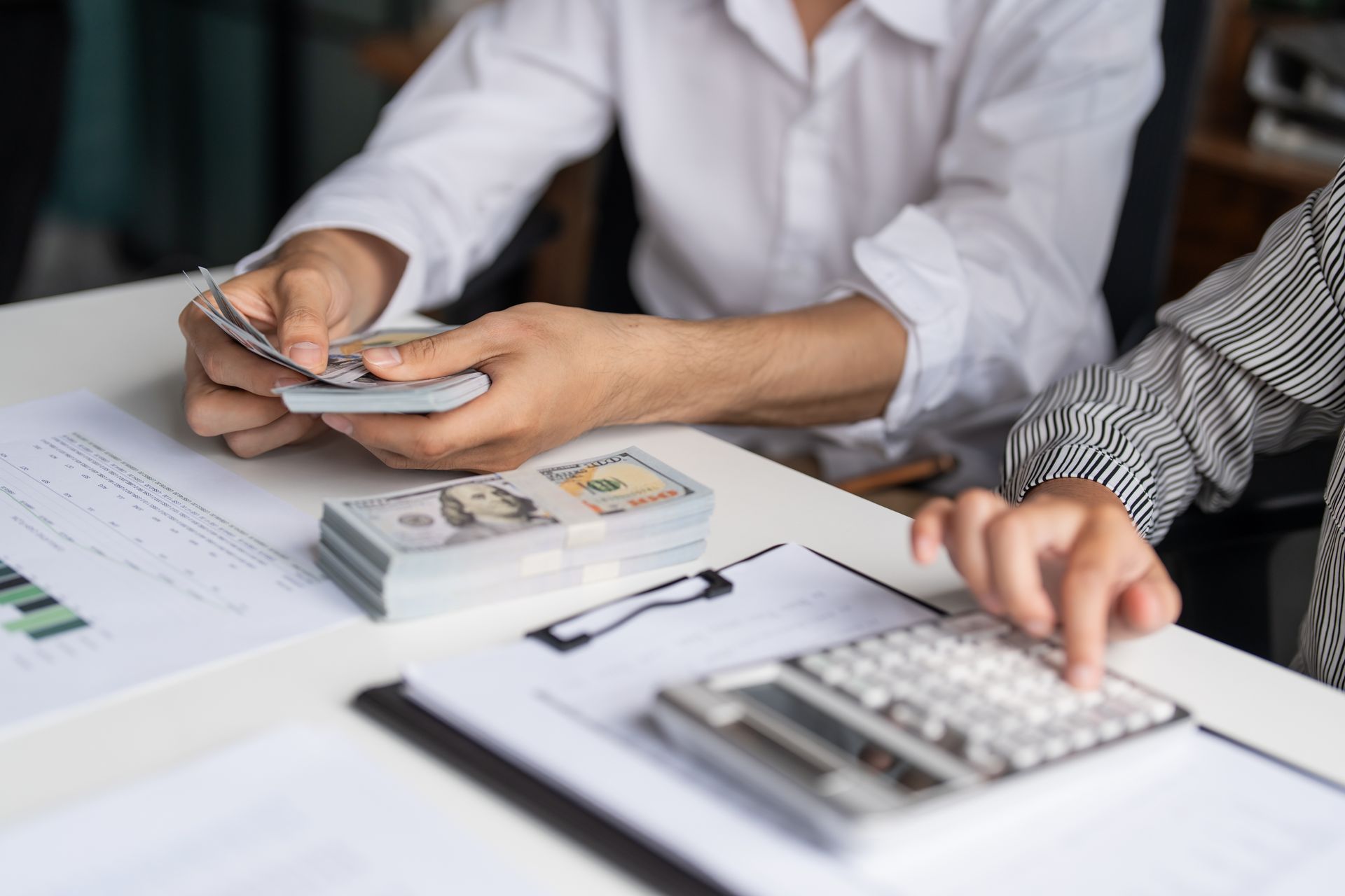 Hands counting cash and using a calculator at a desk with financial documents