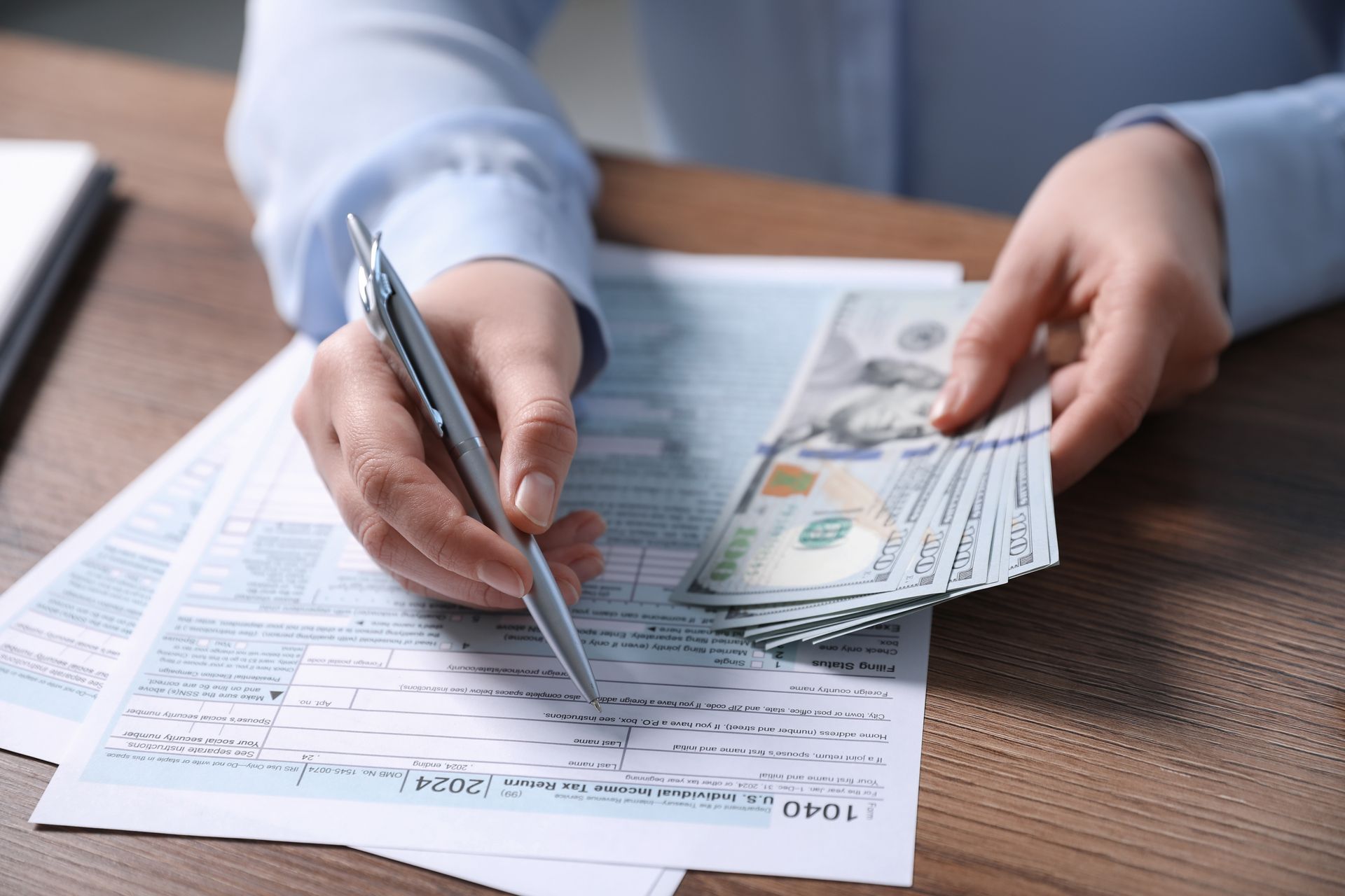 Person signs a document while holding cash on a desk