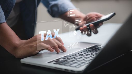 Hands typing on laptop with smartphone nearby and a digital TAX overlay