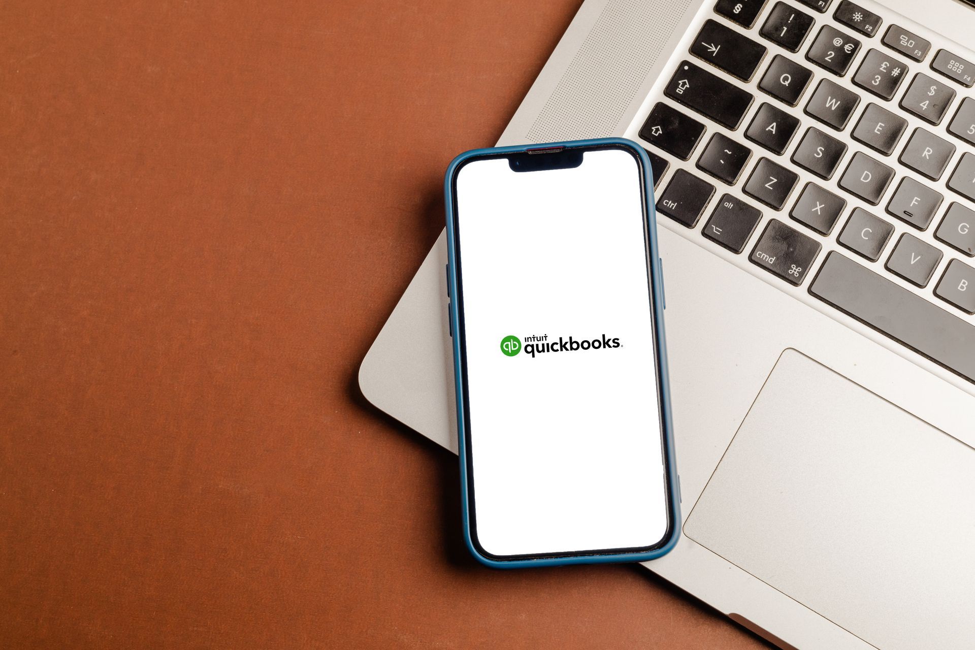 Smartphone on a laptop with a white screen displaying a small green logo on a brown desk