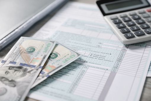 Calculator, banknotes, and pen on a financial document with charts and tables