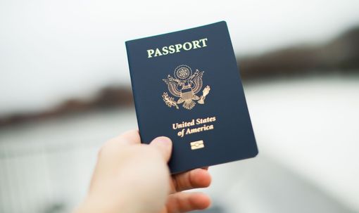 Hand holding a blue U.S. passport outdoors with a blurred background