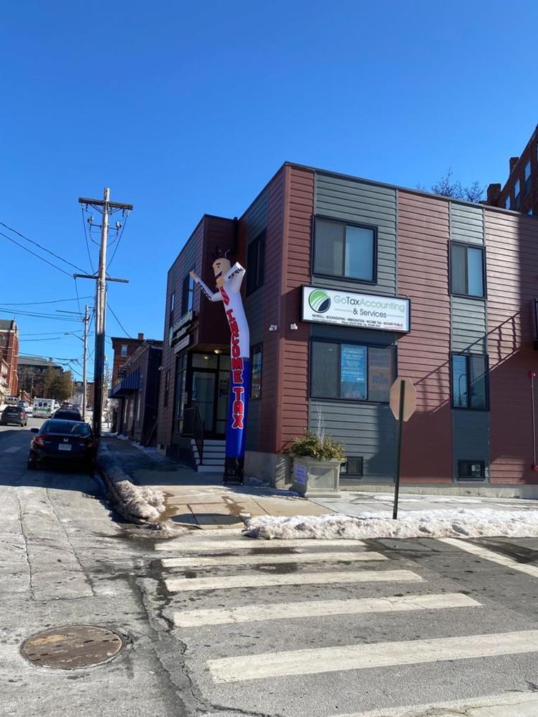 Brick storefront on a sunny street corner beside a crosswalk and parked cars