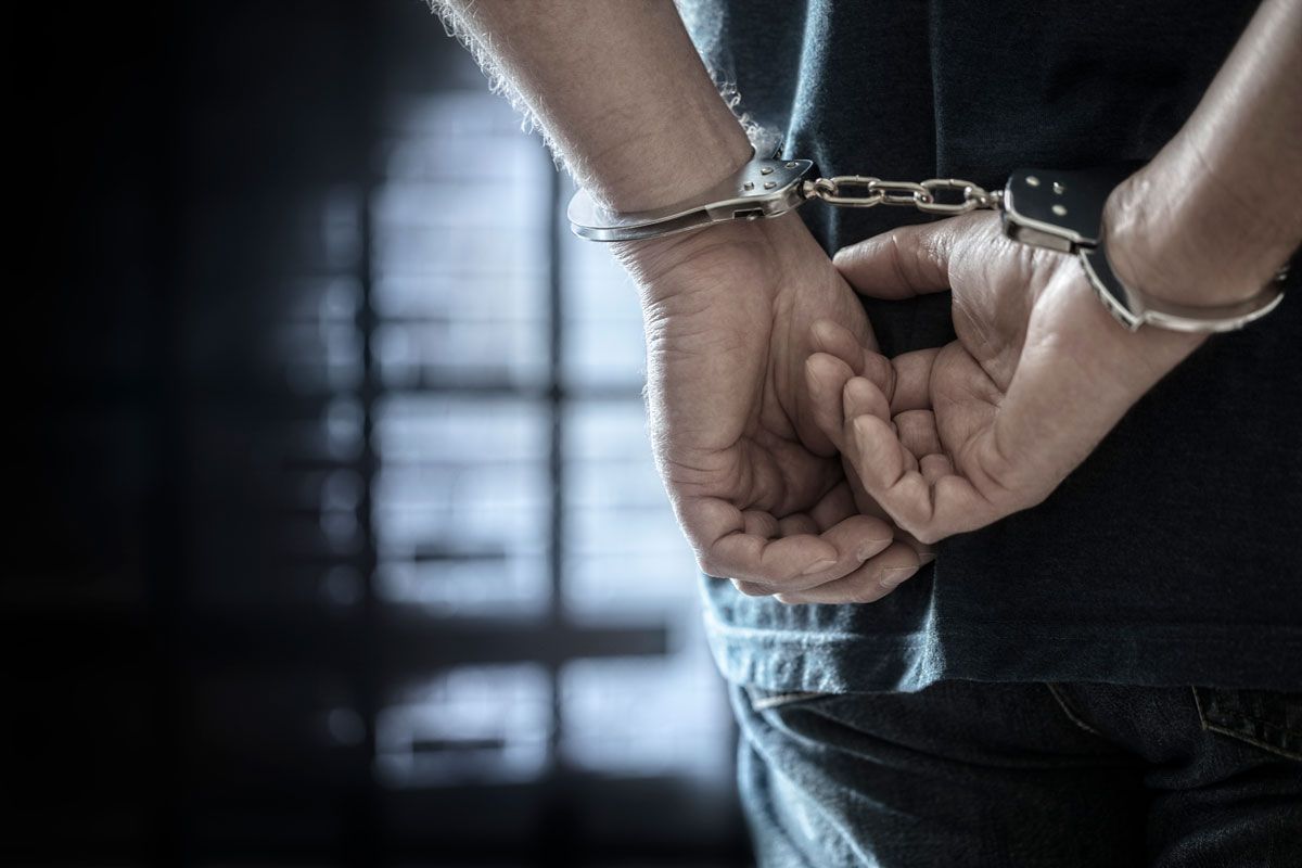 Hands in handcuffs behind a person in a dark room.