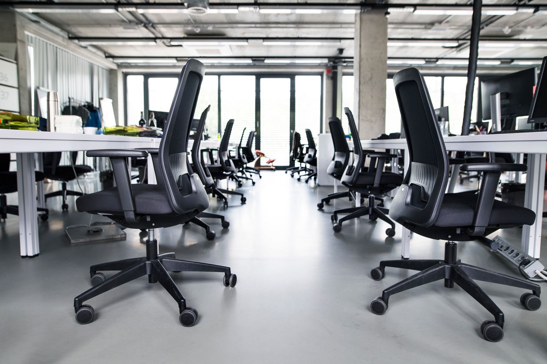 open-plan office with rows of black ergonomic chairs and white desks open-plan office with rows of black ergonomic chairs and white desks