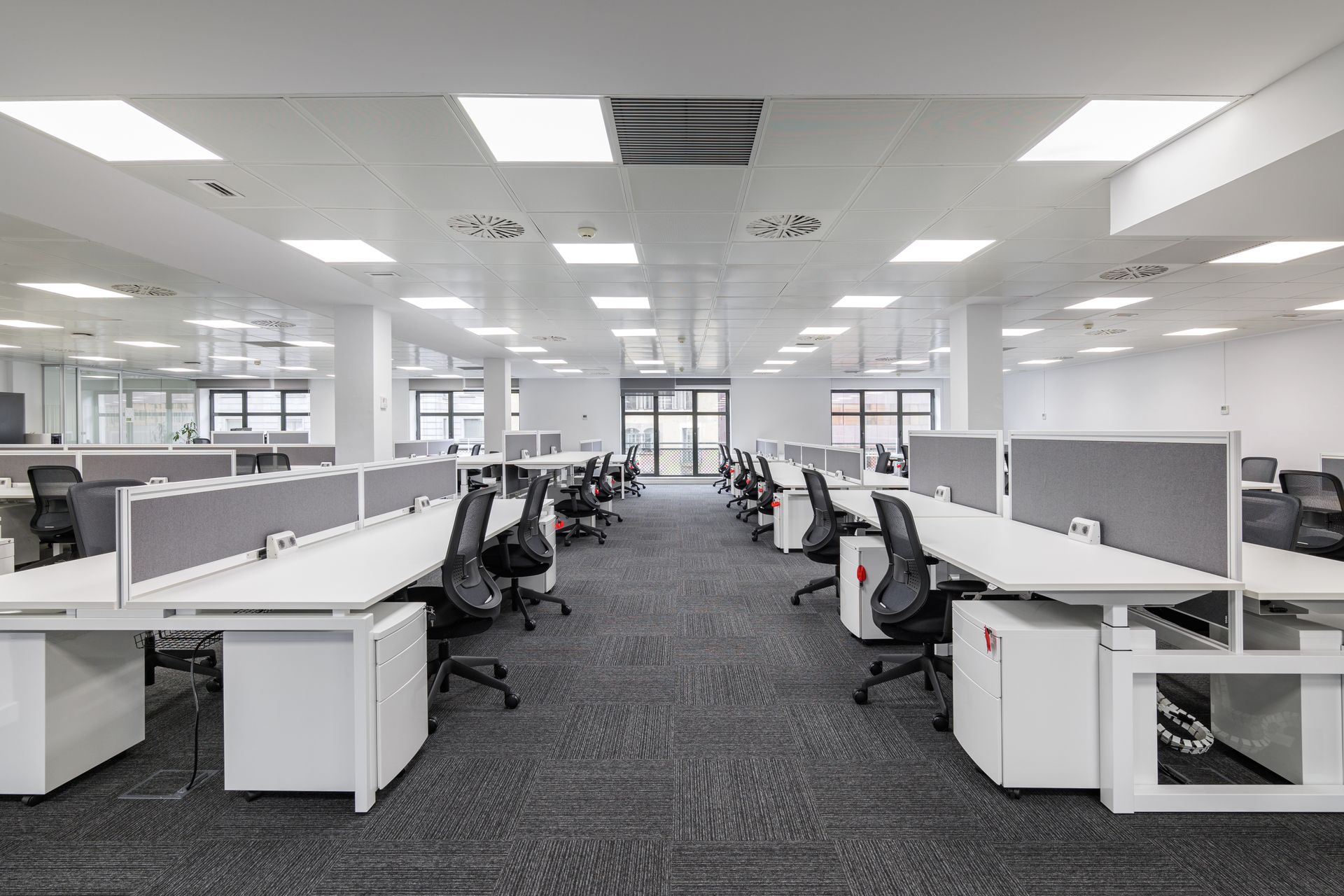 Modern open-plan office with rows of white workstations and black ergonomic task chairs