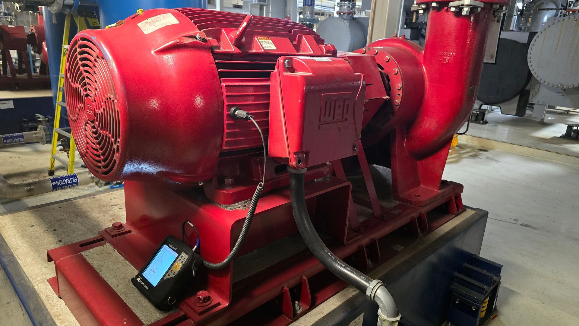 Pompe industrielle rouge avec moteur et panneau de commande sur un socle bleu, en intérieur.