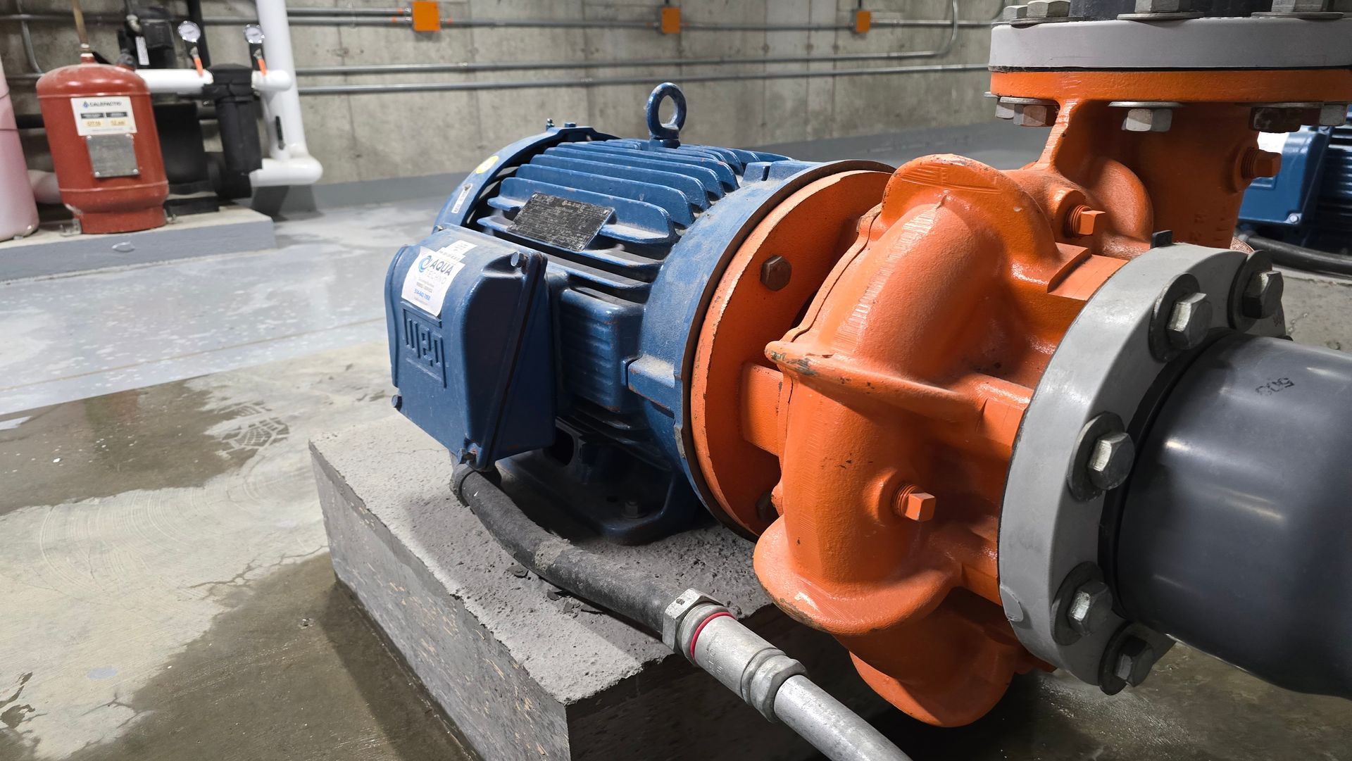 Moteur électrique bleu relié à une pompe orange par des tuyaux, le tout installé dans un environnement industriel.