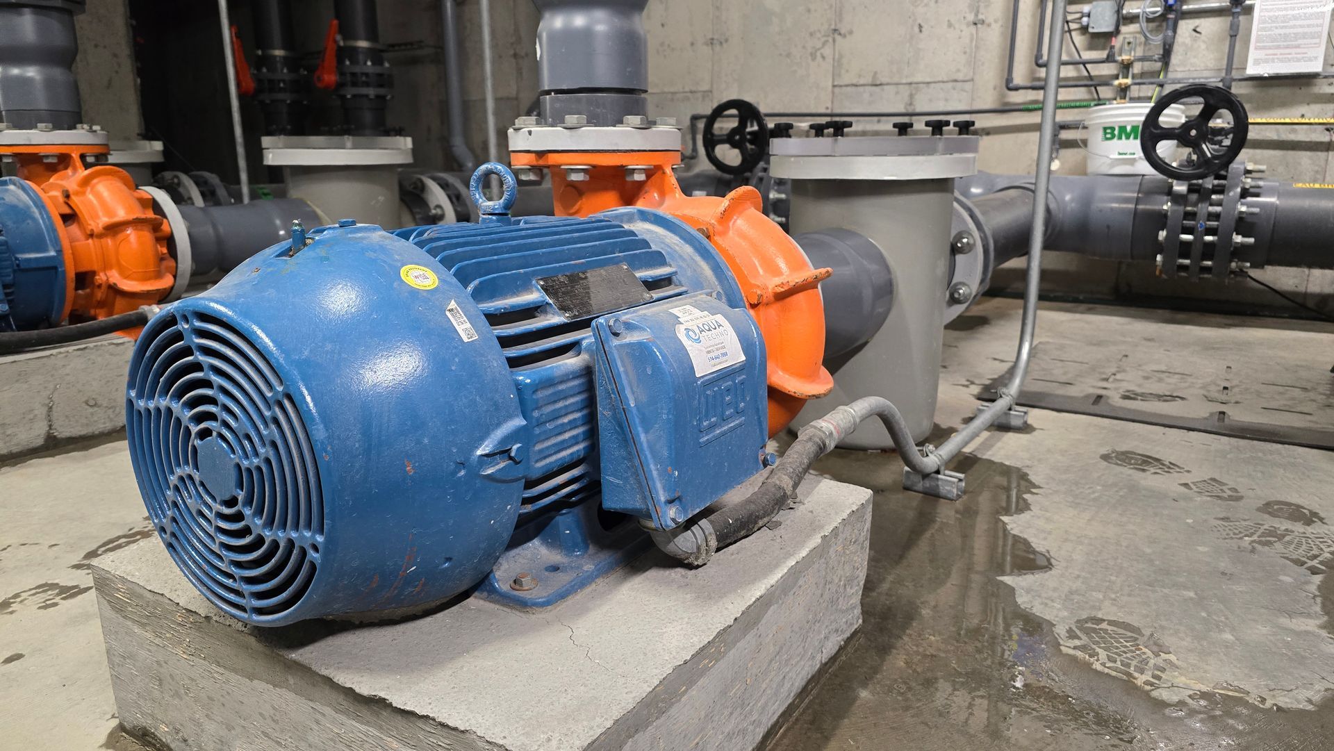 Un moteur électrique bleu avec des composants orange repose sur un bloc de béton dans un environnement industriel.