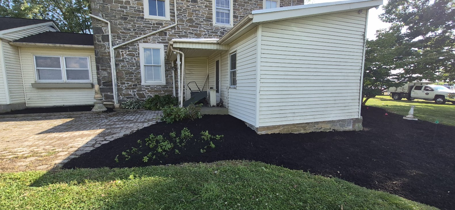 Stone house exterior with white-sided porch, black mulch beds, and green lawn in daylight