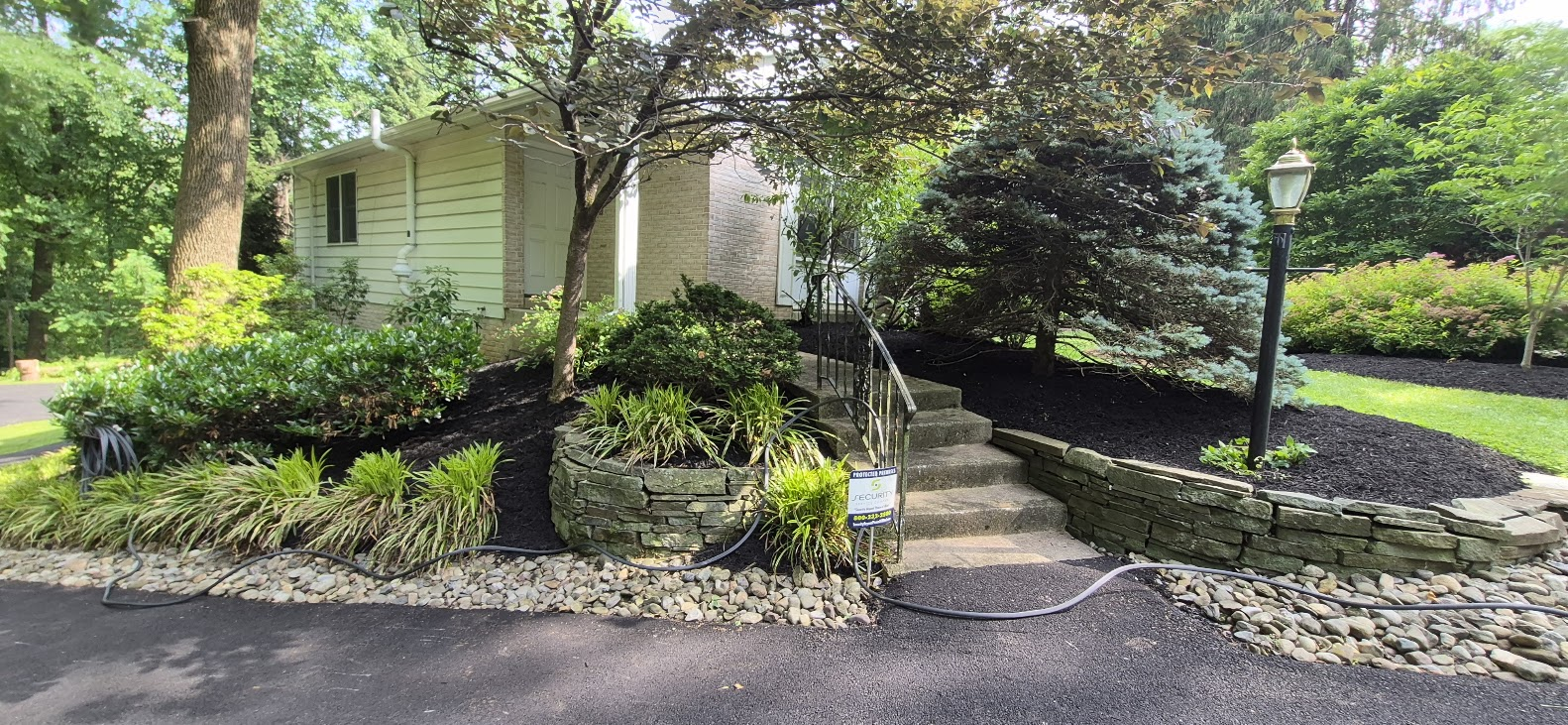 Large stone steps set in a garden with a wooden fence and flowering shrubs in the background.