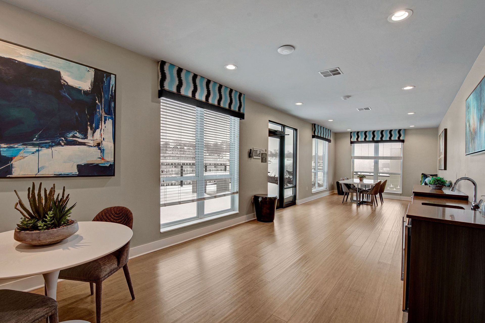 Bright, modern room with light wood floors, large windows, and a dining area with a small round table.