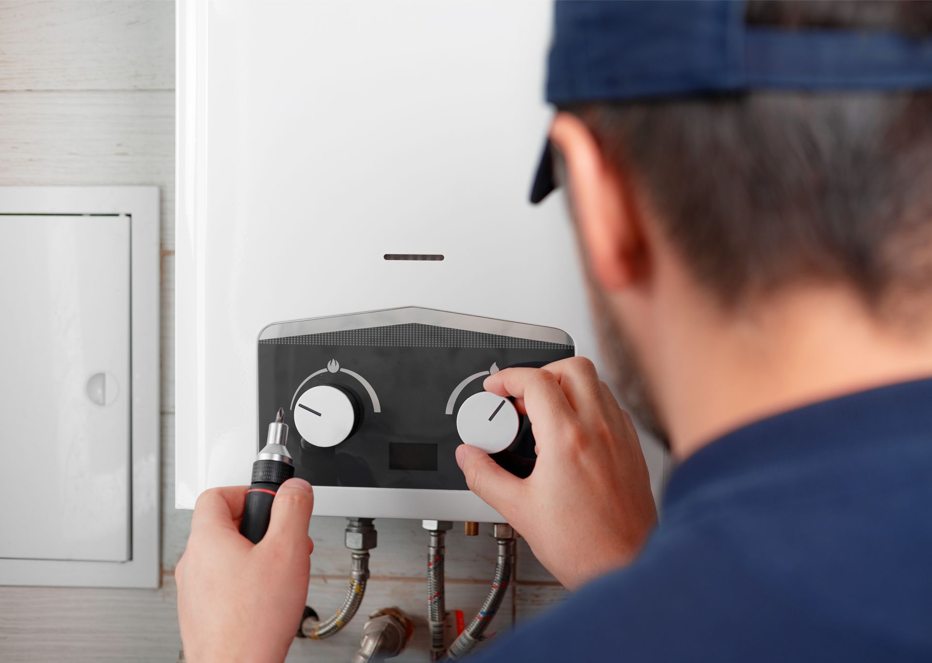 A man is fixing a water heater with a screwdriver.