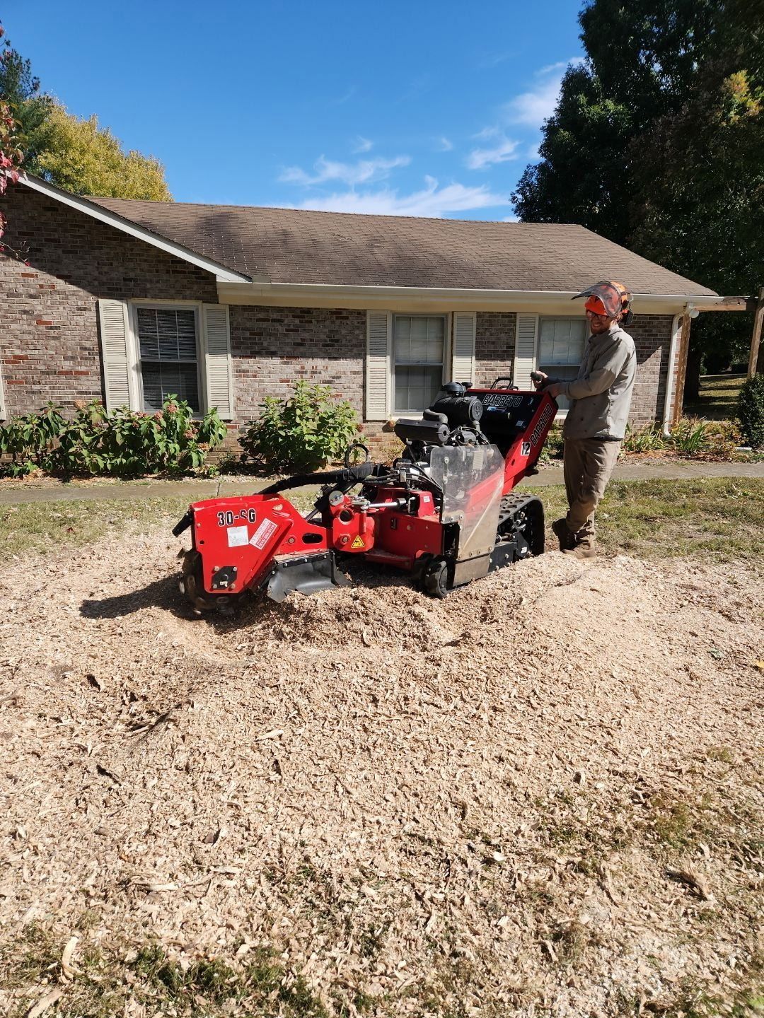 Person operating a red wood chipper in front of a house on a sunny day