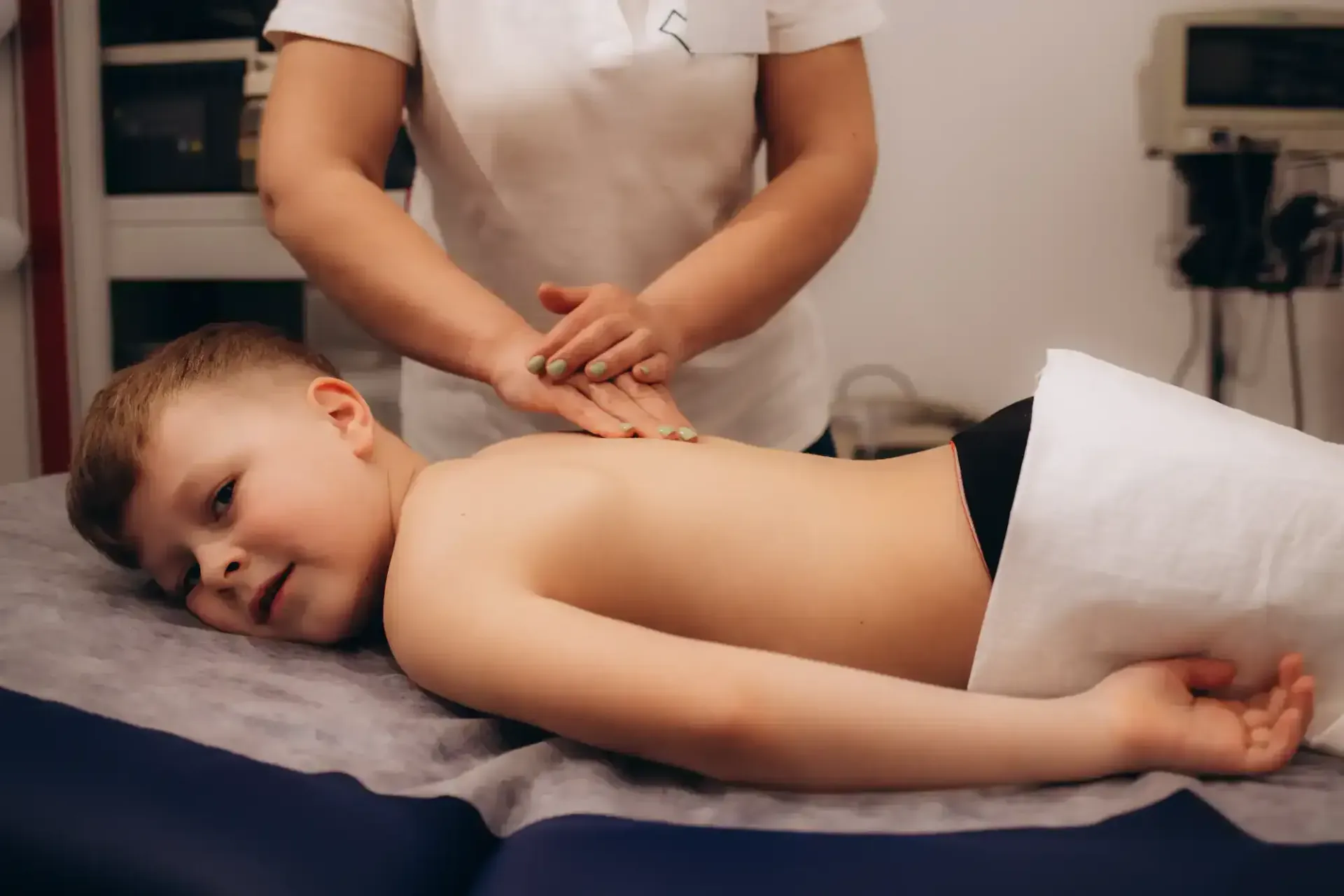 Child lying face down on a massage table while a therapist massages their back