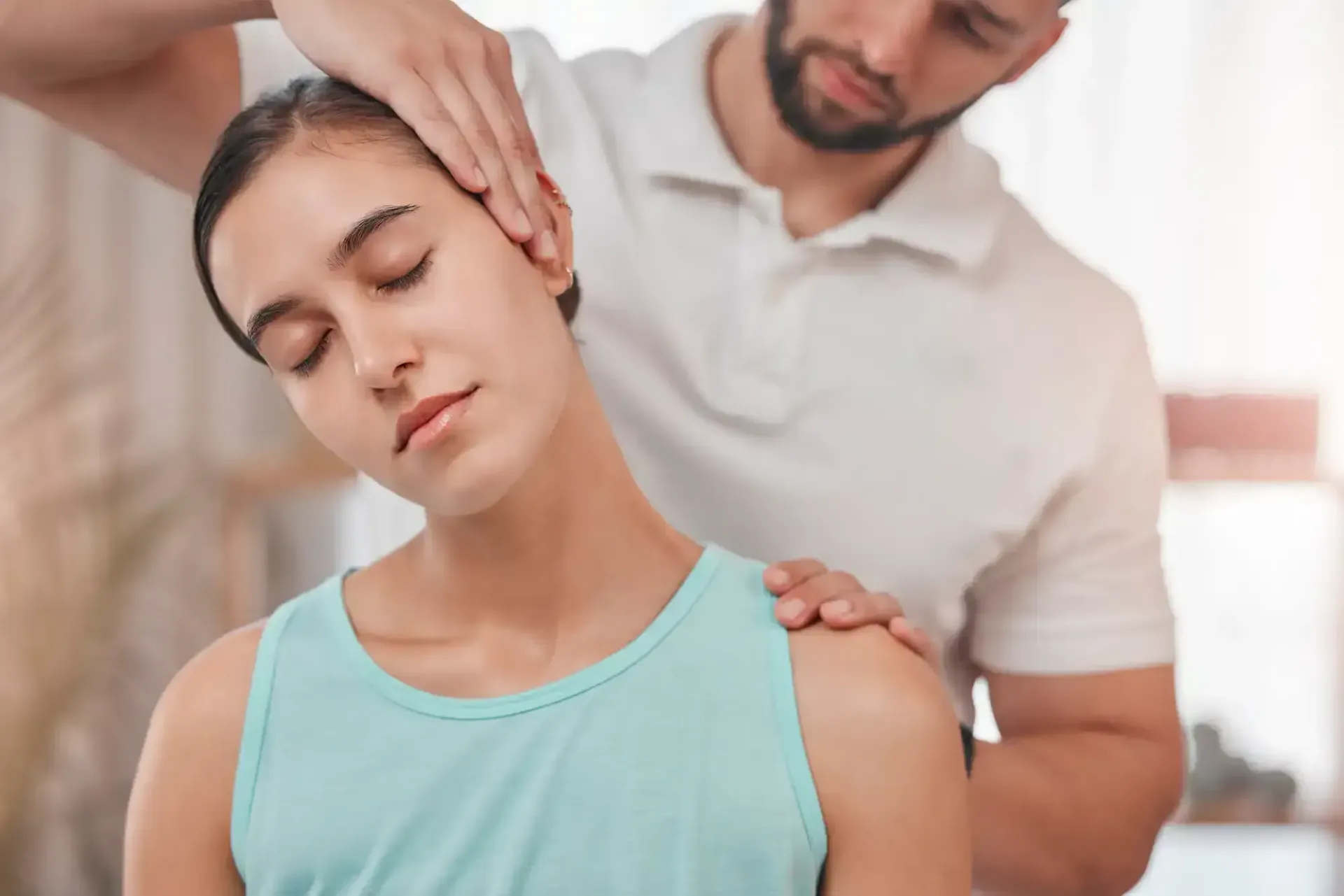 Physical therapist supporting a woman stretching her neck and shoulder in a bright room
