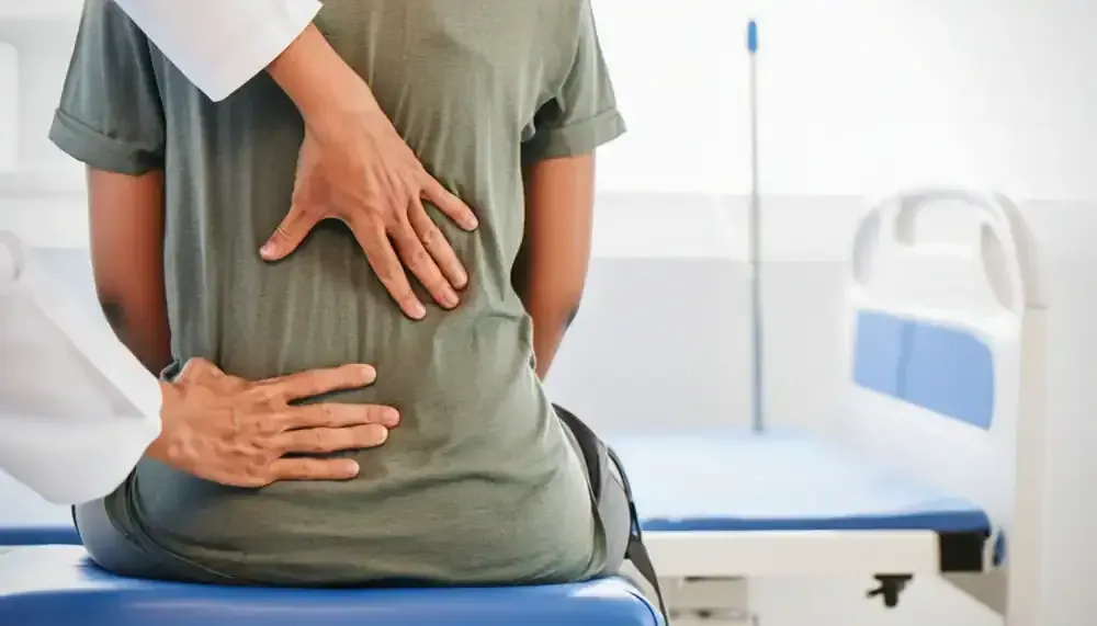 Physical therapist adjusting a patient's lower back while they sit on a treatment table in a clinic