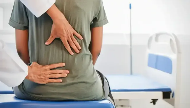 Doctor examining a patient’s lower back in a clinic room
