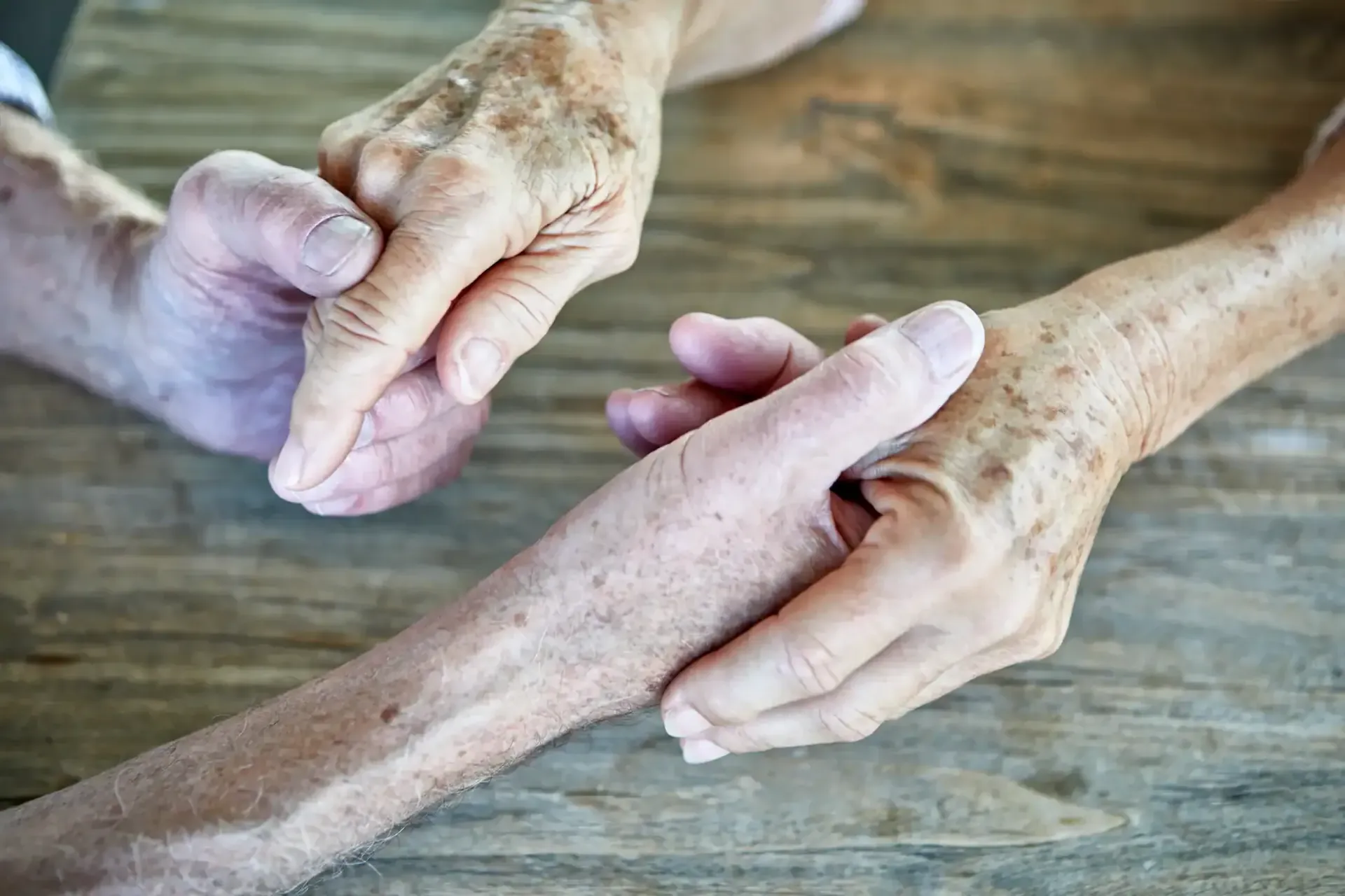 Two hands massaging an elderly person’s forearm on a wooden table