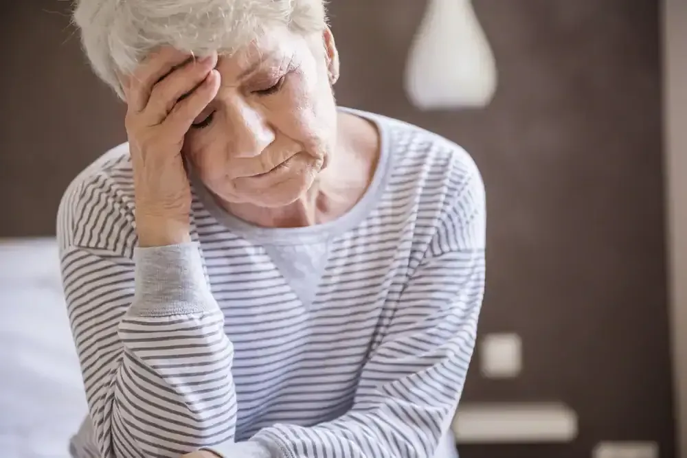 Person holding their forehead with eyes closed, appearing fatigued or in pain indoors.