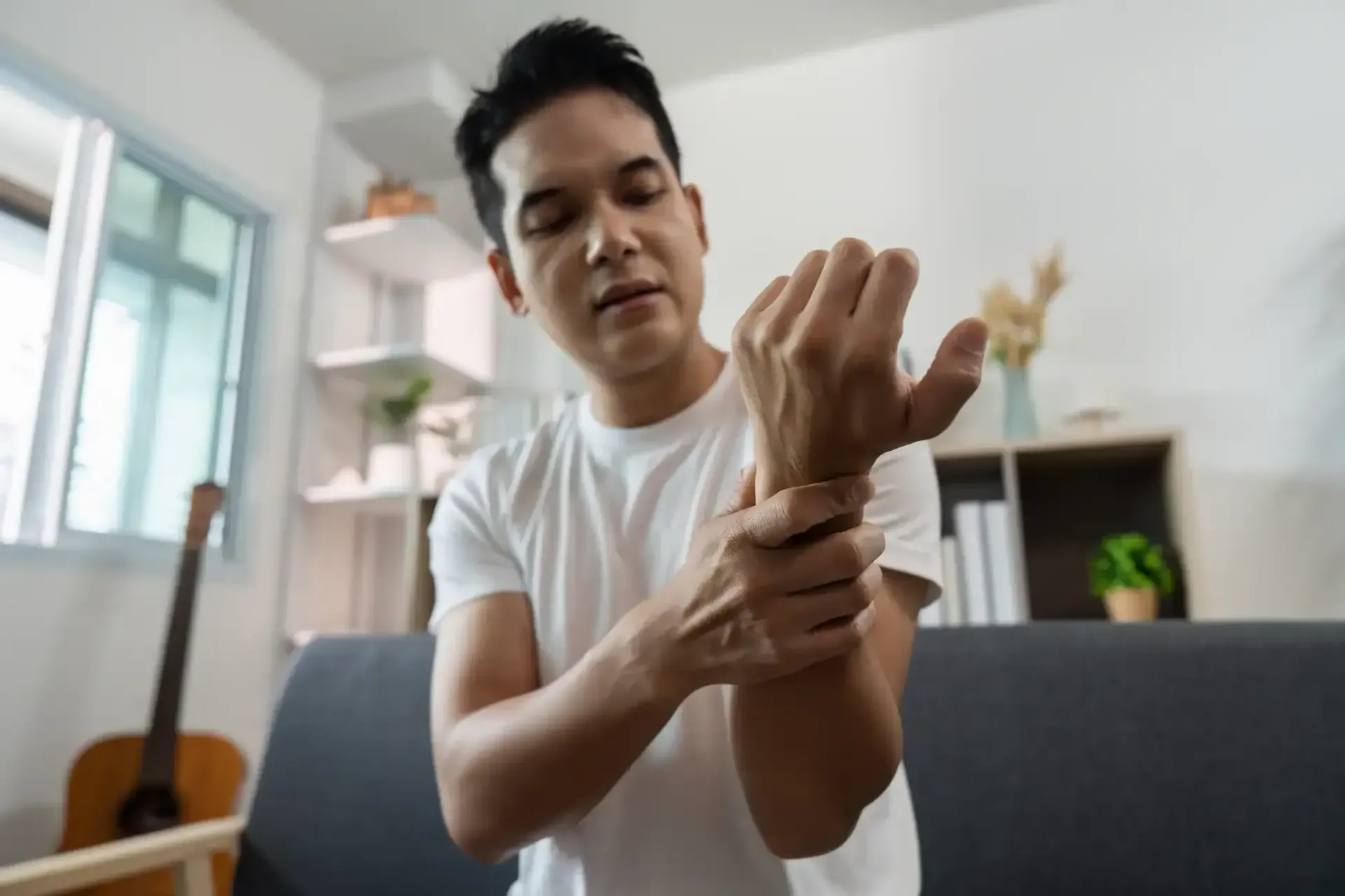 Person rubbing their wrist in a bright living room while seated on a couch