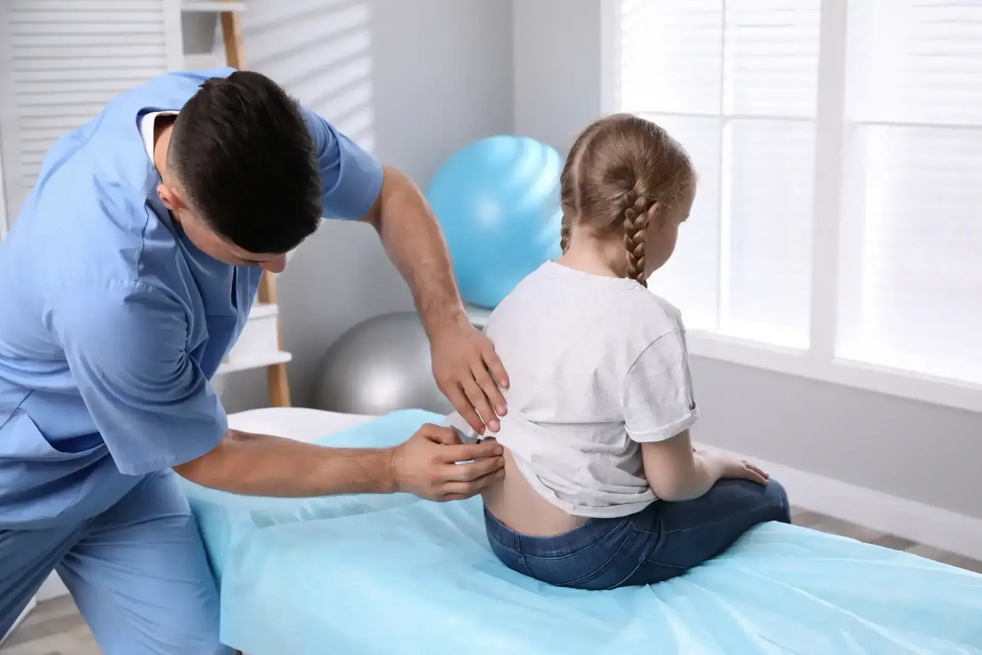 Physical therapist adjusting a child's lower back on a treatment table in a bright clinic room
