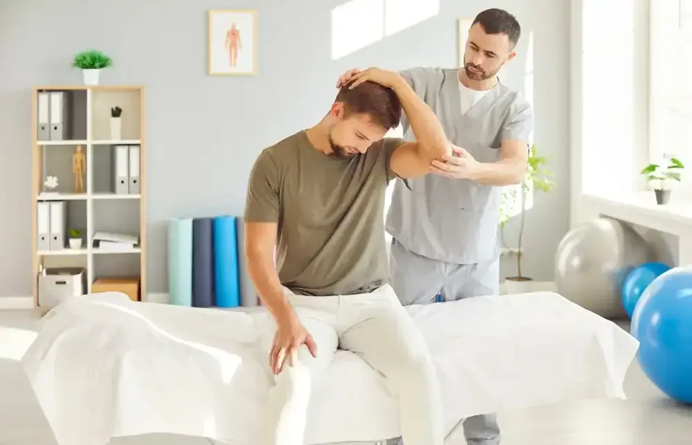 Physical therapist helping a seated patient stretch his neck in a bright clinic room