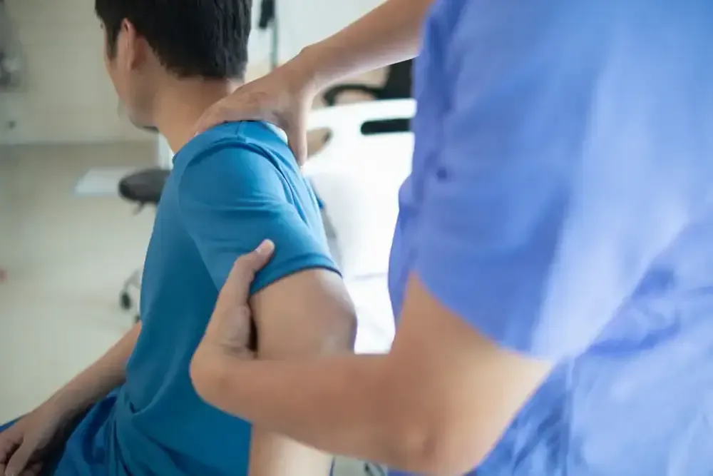 Therapist supporting a seated person’s back and shoulder during a physical exam or massage