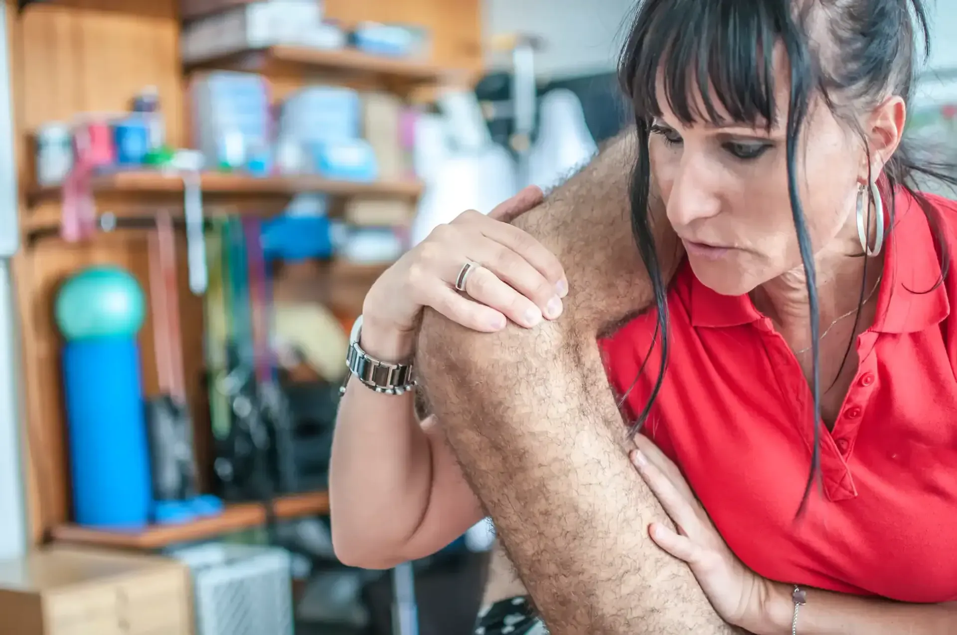 Woman in a red shirt examining a leg injury in a therapy room