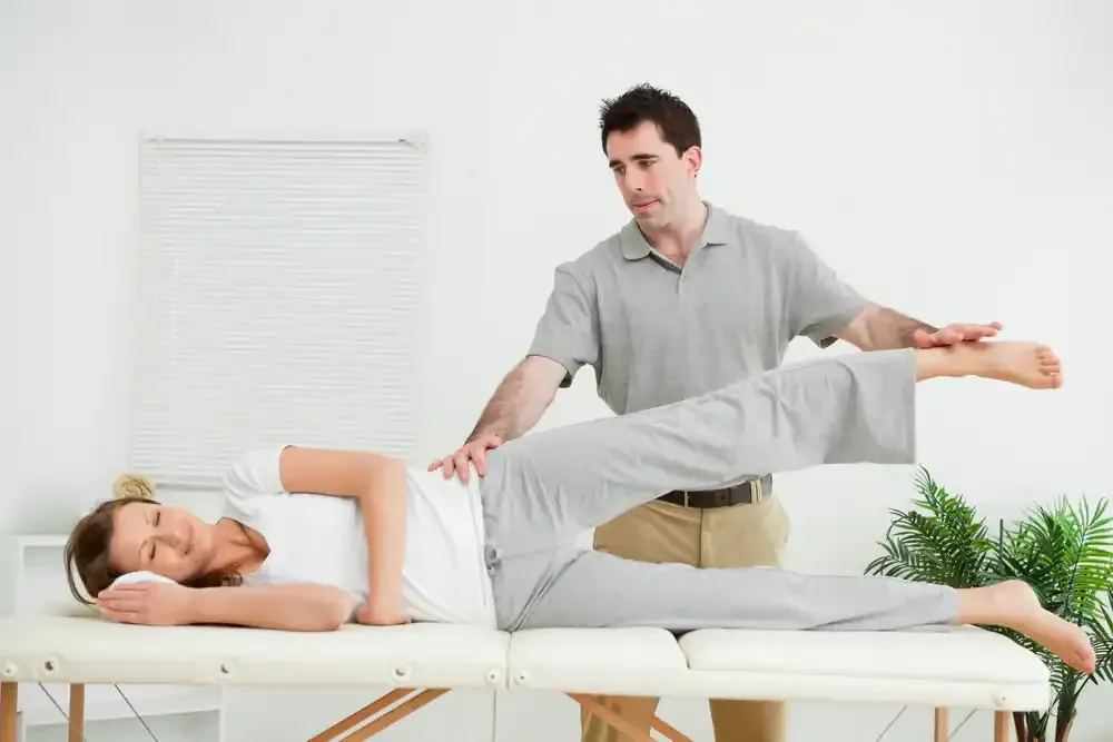 Physical therapist stretching a patient's leg on a treatment table in a bright clinic room