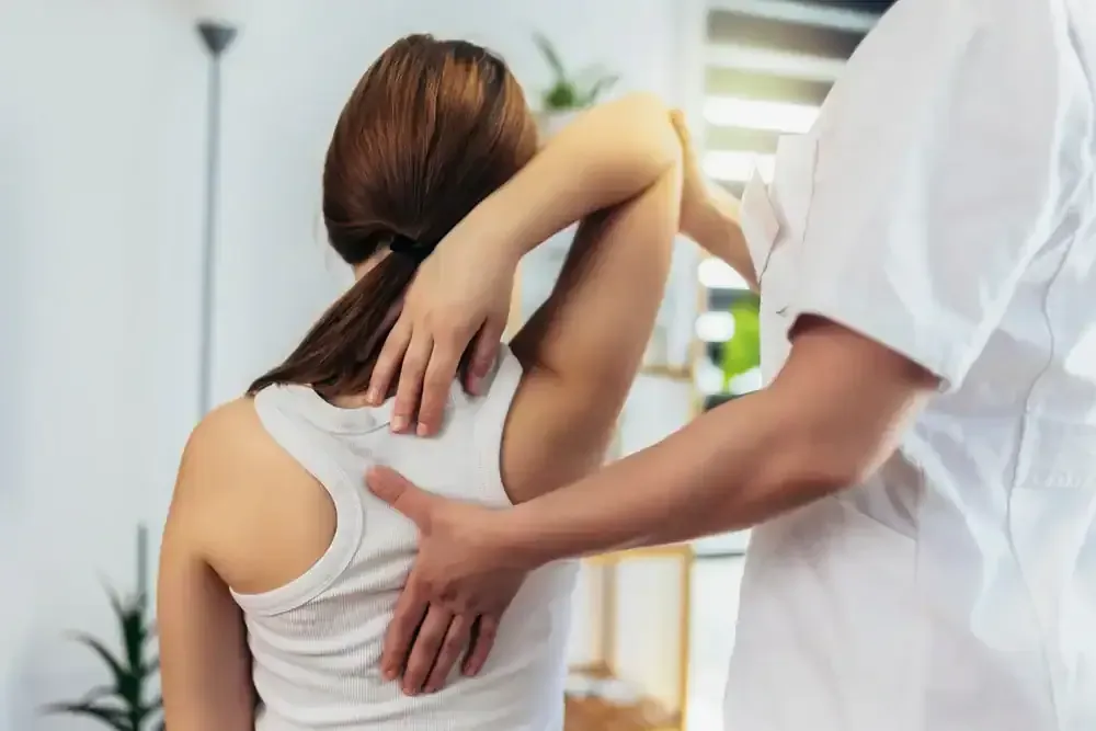 Physical therapist examining a patient’s upper back and shoulder in a clinic