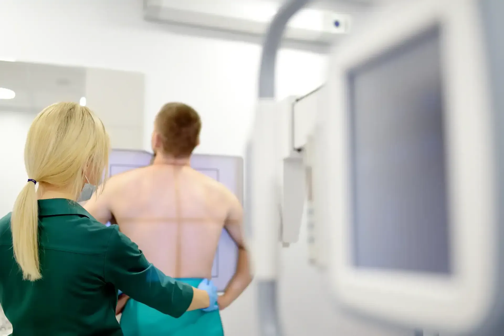 Technician in green gown adjusts a shirtless patient during a medical scan in a clinic.