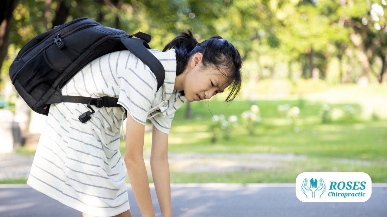Young student with backpack bending forward on a sunny outdoor path, smiling and resting hands on knees.