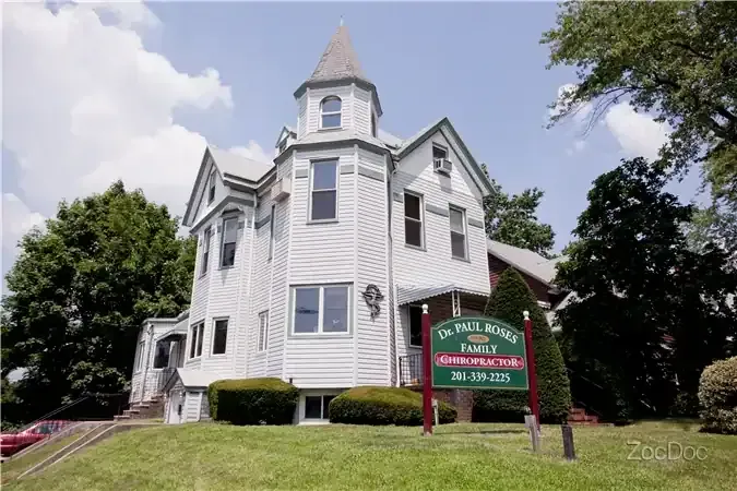 White Victorian house with a red sign reading “Muskegon Area District Library” on a grassy lawn.