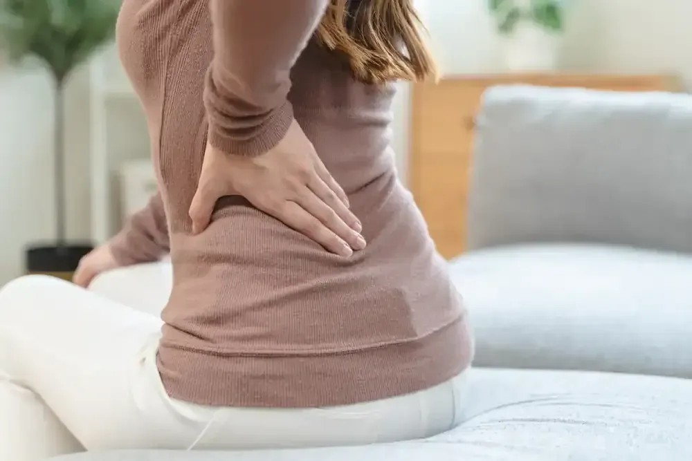 Person holding lower back while sitting on a couch, suggesting back pain