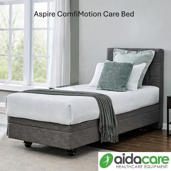 Aspire ComfiMotion Care Bed in a bright bedroom, gray upholstered base with white bedding and green throw blanket
