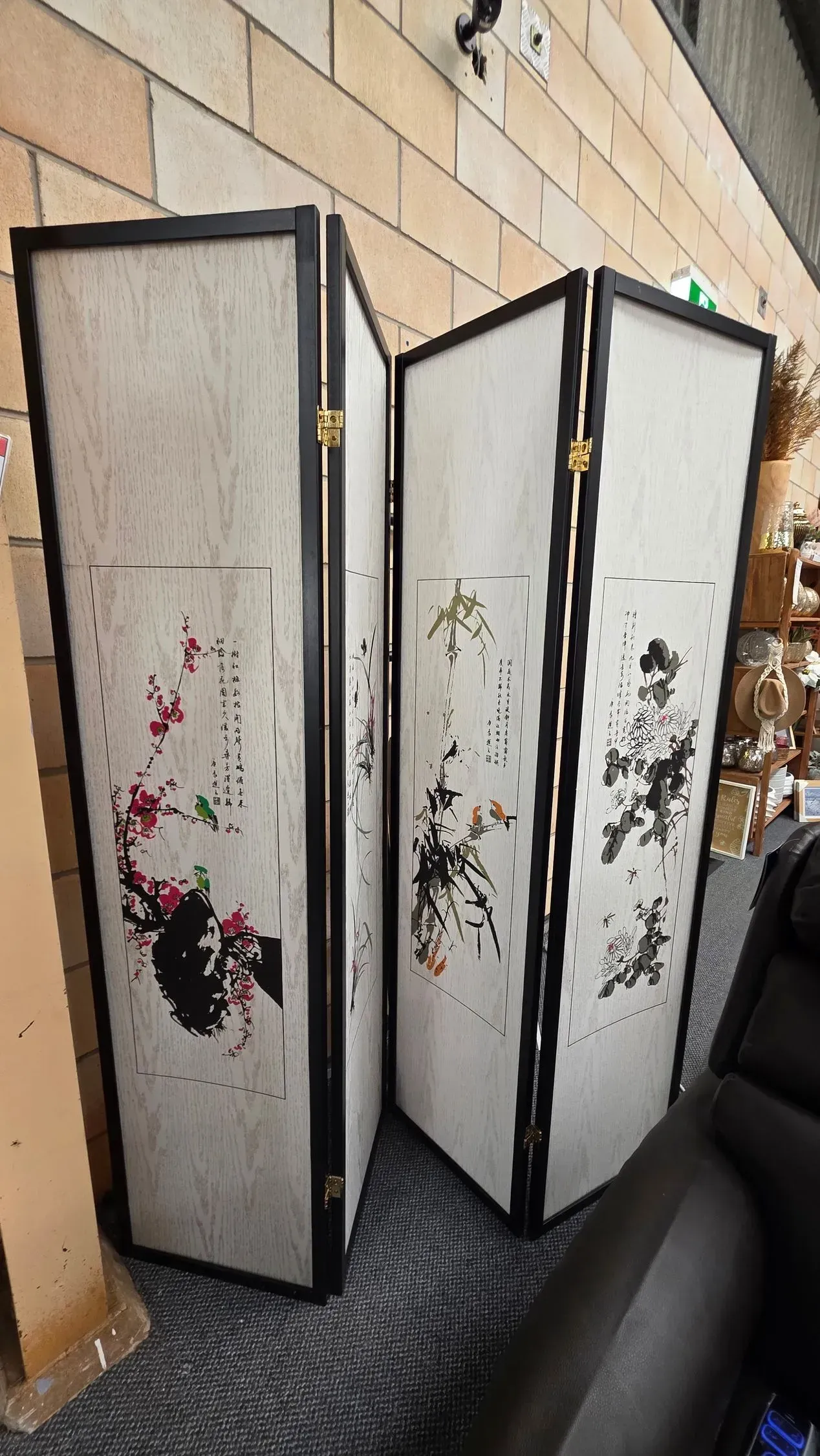 Three-panel decorative folding screen with floral patterns beside a brick wall and sofa