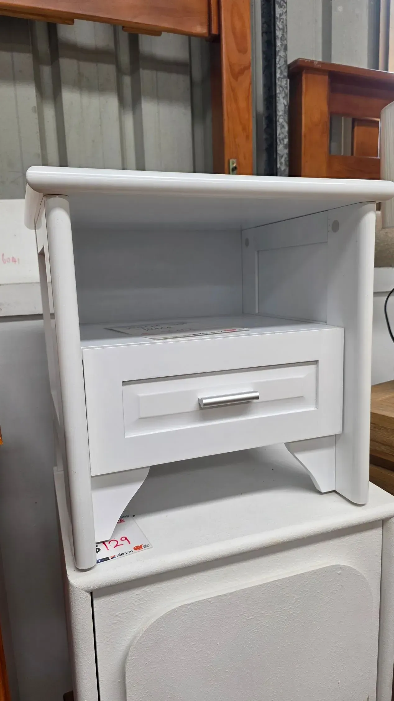 White wooden nightstand or shelf with a single drawer, placed on top of a speaker-like cabinet.
