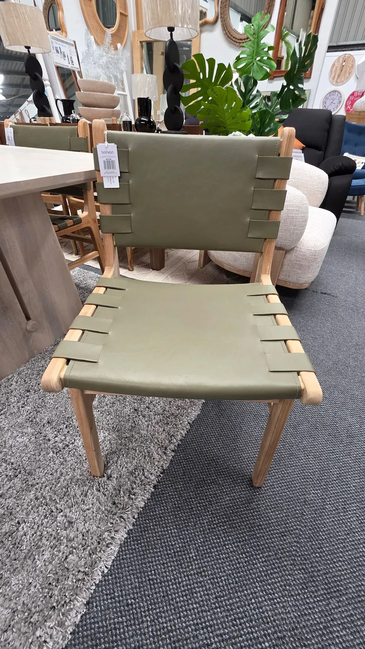 Olive green woven lounge chair with wooden legs on a showroom carpeted floor.