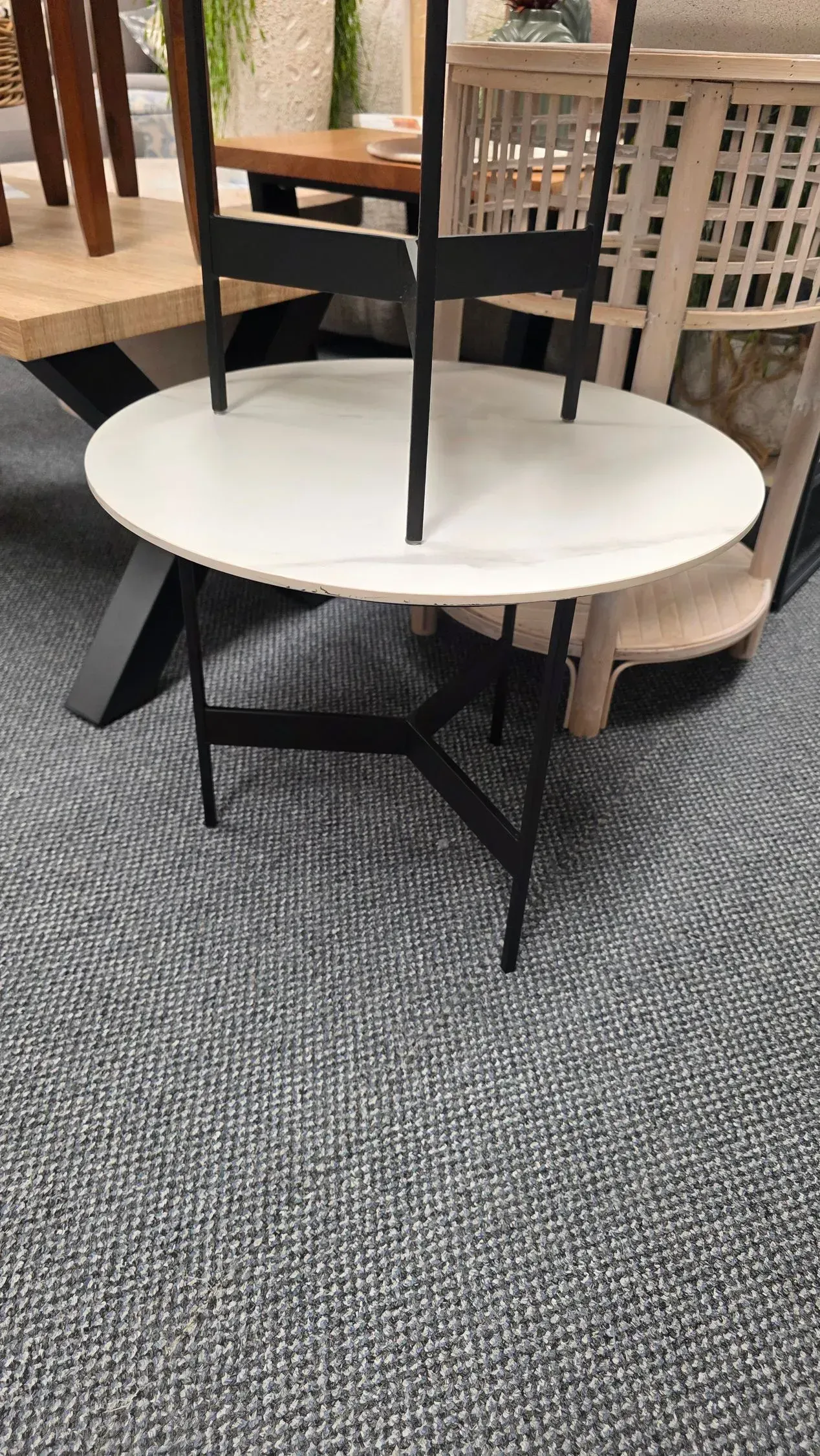 Round white table with black chairs in a carpeted furniture showroom