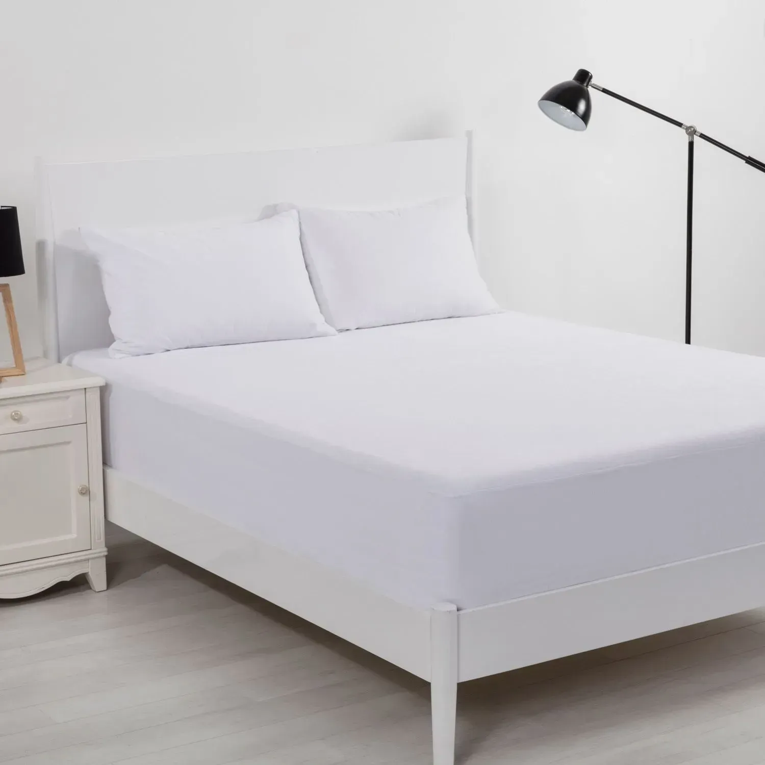 Minimalist white bed with pillows, bedside table, and floor lamp in a bright bedroom