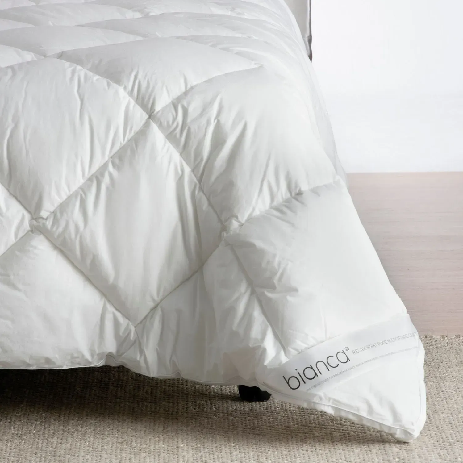 White quilted comforter draped over a bed, with a small “bianca” label visible on the corner.