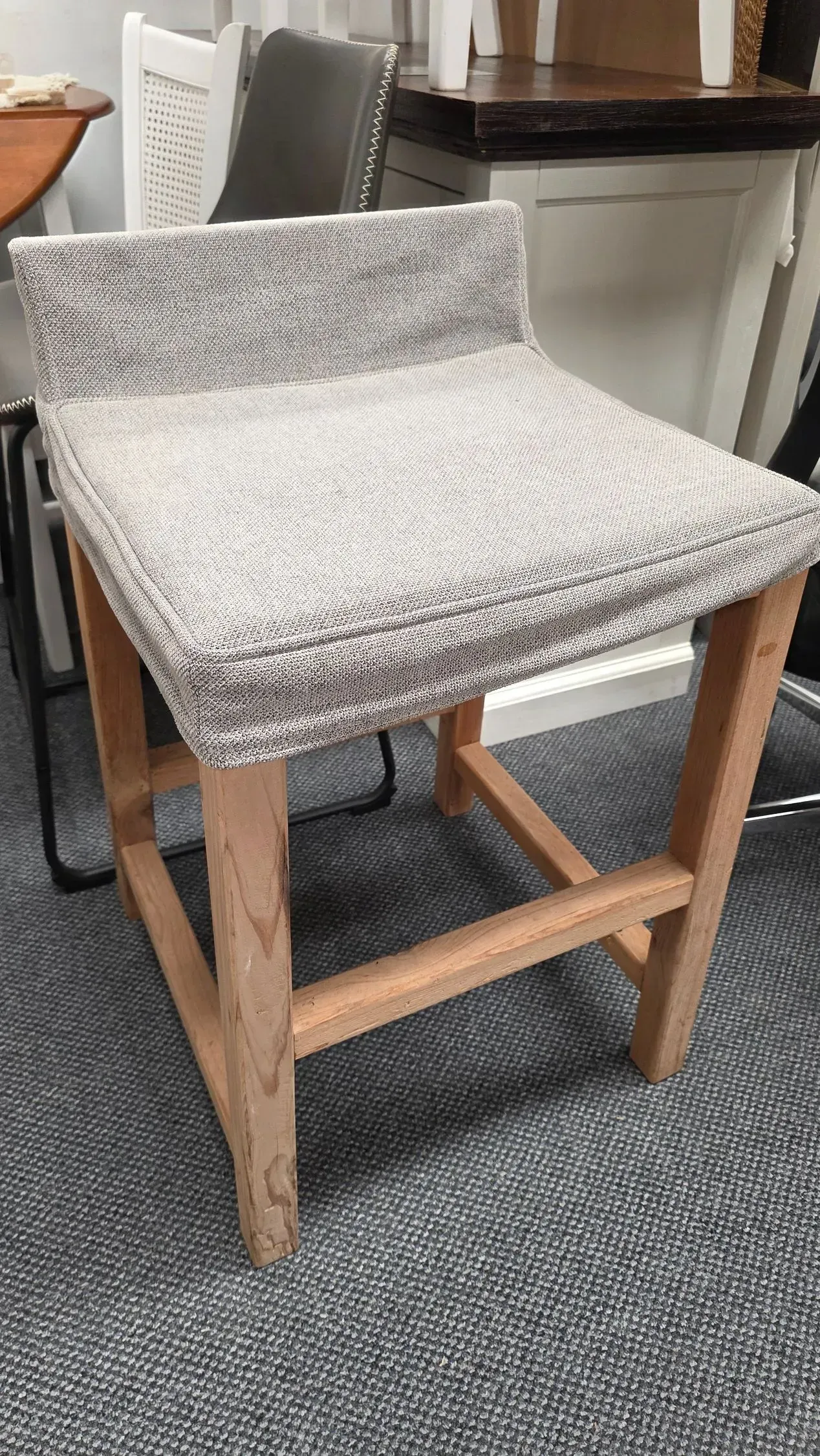 Gray upholstered bar stool with wooden legs on a dark woven rug indoors