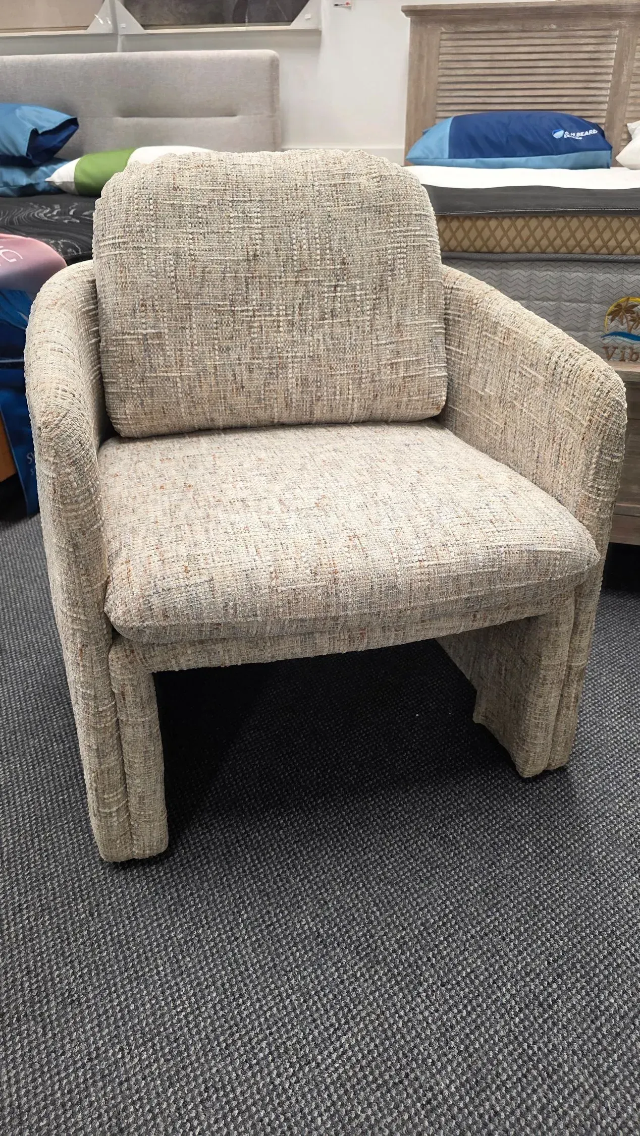 Beige upholstered armchair on a carpeted floor in a furniture showroom.