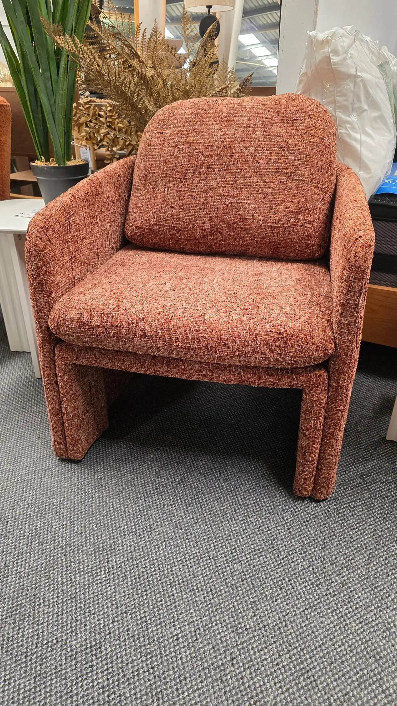 Rust-colored textured armchair on a gray carpet in a showroom.