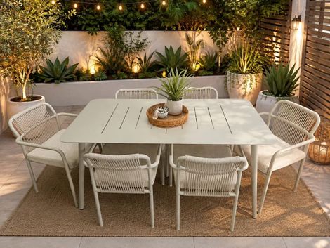 Cozy outdoor dining area with a white table, wicker chairs, and warm string lights at night