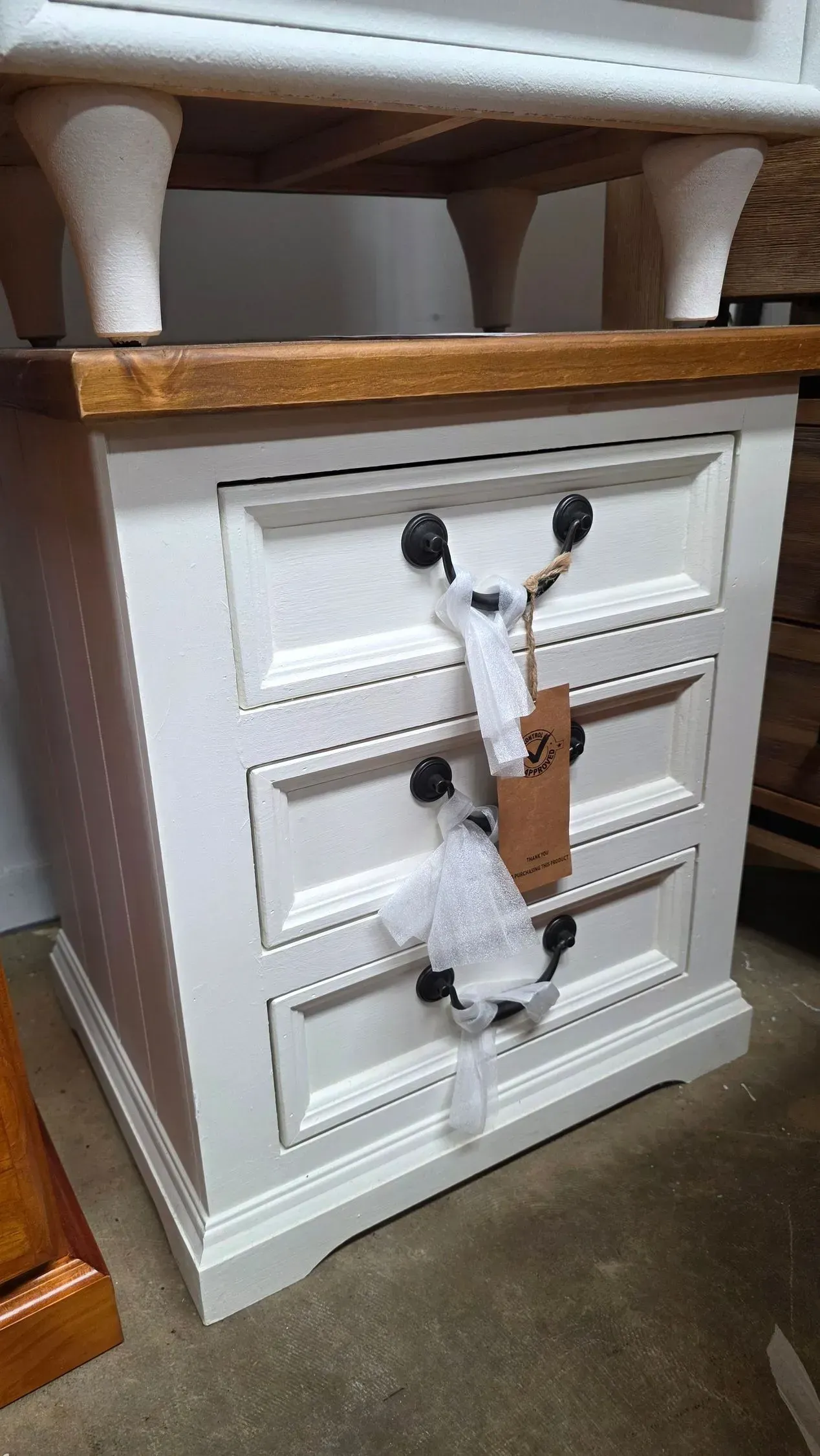 White cabinet with carved drawers and a giraffe-face handle, under a wooden shelf on a carpeted floor
